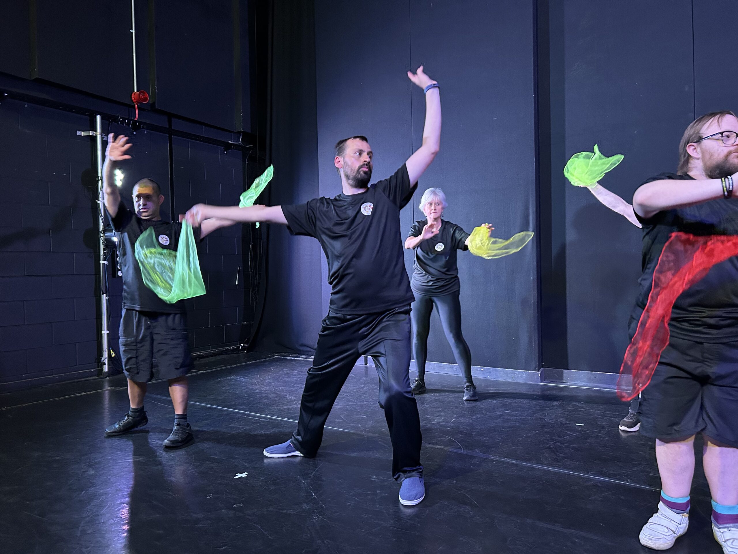 A group of dancers in black, with their arms in the air, holding dance cloths as props for their routine.