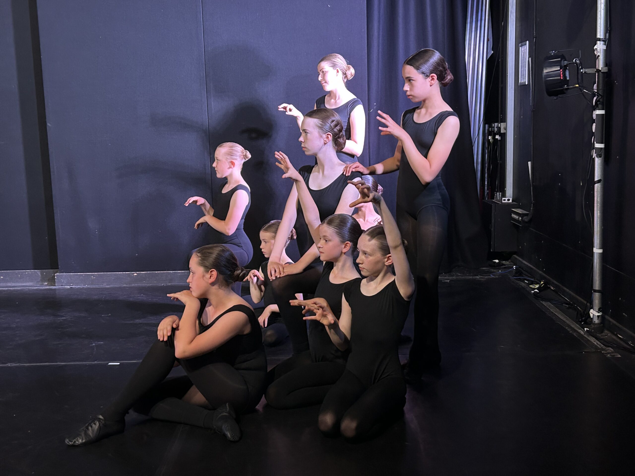 A group of young dancers, all in black with claw hands in front of their bodies.